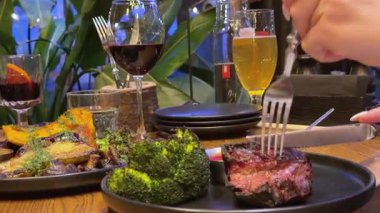 Patates ve brokolili kaburga bifteği ve bir bardak kırmızı şarap, dışarıda yemek, biftek, orta pişmiş. 4k görüntü