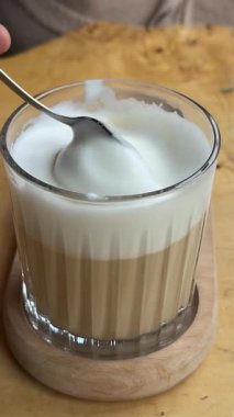 Kadın kahvaltıda kahveci dükkanında dekoratif köpüklü kahve içiyor. Dişi, tahta masada içecekten köpük damlayan kaşığı alır. Yüksek kalite 4k görüntü