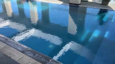 Yüzme havuzunda parlak yansımalı mavi su, güzel güneş ışığı yansımaları ve hafif dalgalarla dolu bir yüzme havuzunda açık mavi suya yakın çekim. Rahatlatıcı yaz.