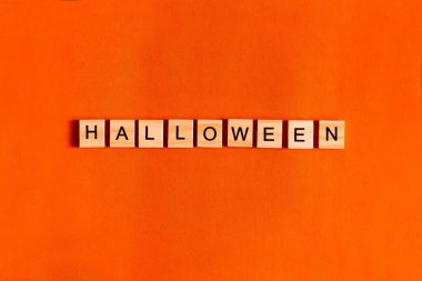 Siyah kağıt siluetler, yarasalar, balkabağı, örümcek içeren turuncu arka planda Cadılar Bayramı harfleri. Cadılar Bayramı Konsepti. Yukarıdan görünüm