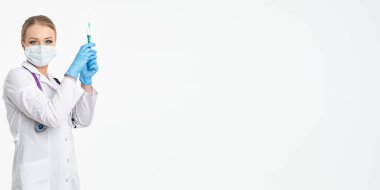 Maskeli ve beyaz önlüklü genç bir hemşire şırınga tutuyor. İğne yapmak için, grip aşısı olmak için. Aşı ve gribe karşı korunma kavramı, bir salgından. kopyalama alanı. Pankart