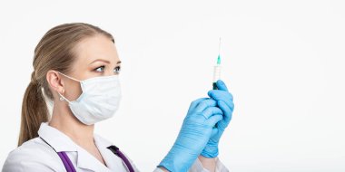 Maskeli genç hemşire aşıyı bir hastanenin yanında otururken şırıngaya çeviriyor. Kadın hasta grip enjeksiyonunu bekliyor. Aşı kavramı ve gribe karşı koruma