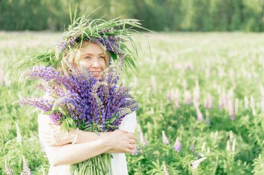 Elinde bir buket kır çiçeği tutan hippi bir kız. Kız yüzünü lupin buketinin arkasına sakladı. Kız çiçek tarlasında büyük bir buket mor lupin tutuyor. Doğa konsepti. Burada.