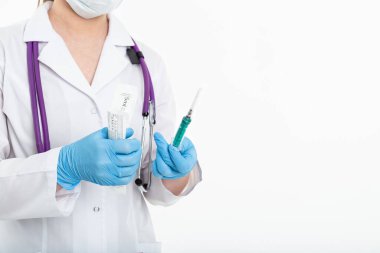 Maskeli genç bir hemşire beyaz önlüklü beyaz arka planda bir şırınga açar. Aşı yapmak için, iğne yapmak için. Aşılama ve gribe karşı koruma kavramı, hırslı, kopyalama alanından