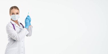 Maskeli ve beyaz önlüklü genç bir hemşire şırınga tutuyor. İğne yapmak için, grip aşısı olmak için. Aşı ve gribe karşı korunma kavramı, bir salgından. kopyalama alanı. Pankart