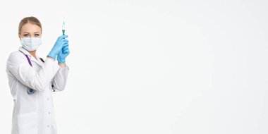 Maskeli ve beyaz önlüklü genç bir hemşire şırınga tutuyor. İğne yapmak için, grip aşısı olmak için. Aşı ve gribe karşı korunma kavramı, bir salgından. kopyalama alanı. Pankart