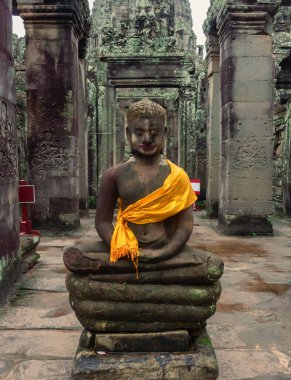 Bayon Tapınağı 'ndaki taş tapınak harabeleri boyunca sarı eşarplı Buda heykeli. Angkor Wat tarihi sitesi, Siem Reap, Kamboçya