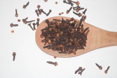 Beyaz arka planda tahta kaşıkta kuru karanfil tomurcukları. Aromatik baharat