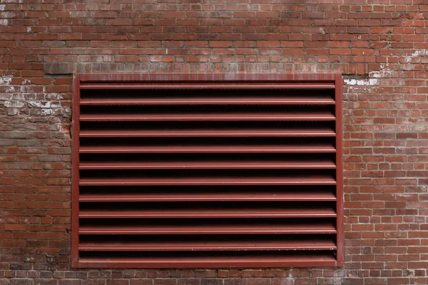 Exterior red brick wall with large painted industrial vent, weathered commercial building, horizontal aspect