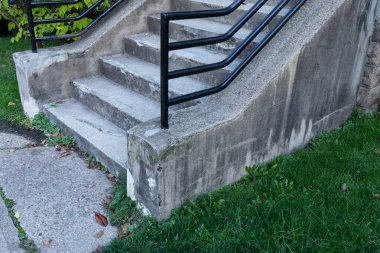 Ağır siyah korkuluklu eskimiş beton merdivenler, çimenli bahçe ve beton yürüyüş yolu, yatay görünüm