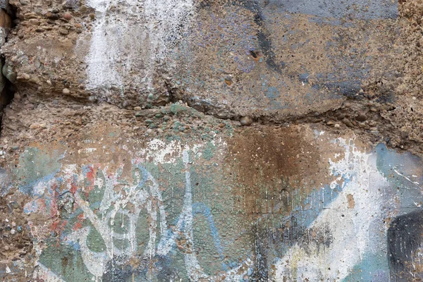 Crumbling concrete aggregate wall with traces of paint in blue, green, and white, horizontal aspect