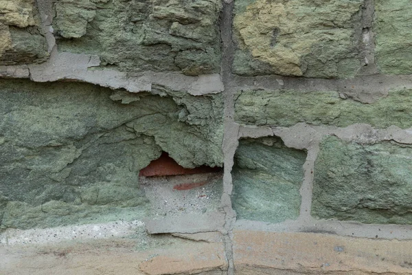 Altındaki tuğlayı göstermek için yenen yeşil kireçtaşı duvar, bozulma ve kirliliğin etkileri, yatay görünüm