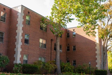 Geniş, eski bir apartmanın gölgeli tarafı beton kiremitli, yatay görünümlü tuğladan bir apartman.