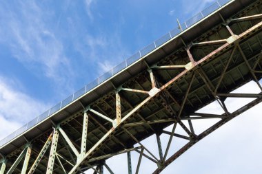 Bir kemer köprüsünün altında paslanmış, çürüyen altyapı, bulutlu mavi gökyüzü, yatay görünüm