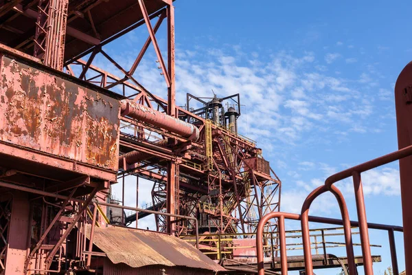 Expansive industrial steel manufacturing facility, rusted beams and girders, vivid blue sky, horizontal aspect