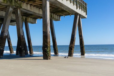 Large concrete pier seen from beneath, blue sky and calm ocean waters, Tybee Island Georgia, horizontal aspect clipart