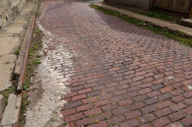 Eski kırmızı tuğla cadde, her iki tarafında da harap beton kaldırımlar, paslı metal kaldırım, yatay görünüm.