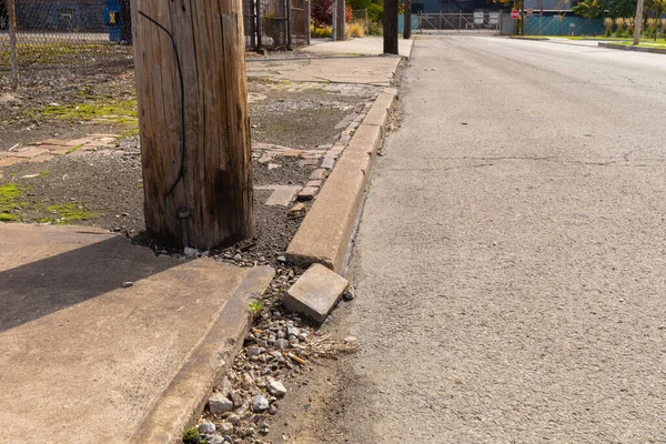 Yıkılmış kaldırım ve asfalt sokağıyla çevrili ahşap elektrik direği endüstriyel bir alanda, alçak görüş, yatay görünüm