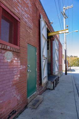 Eski bir kırmızı tuğla ticari binanın kaldırımı ve cephesi, yükleme iskelesi açık sallanan kapılar, dikey görünüm