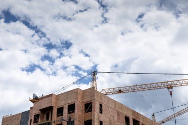 Büyük inşaat vinçleri kontrplak kaplı bir bina yapısının üzerinde, mavi gökyüzü fırtına bulutları, yaratıcı kopya alanı, yatay görünümü