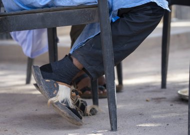 Açık hava ortamında masanın altına takılmış saç derisi detaylarıyla geleneksel Fas sandaletleri. Doğal saç aksanlı el yapımı deri sandaletler, günlük sokak kültürünü yakalıyor..