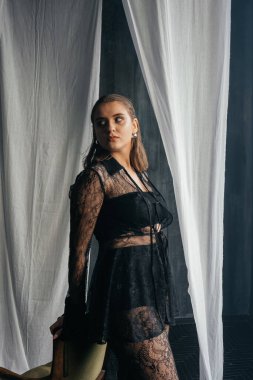 Saf siyah dantelli, kendine güvenen kadın beyaz perdeler arasında duruyor, somut güç, zarafet ve modern gotik moda. Yüksek kalite fotoğraf