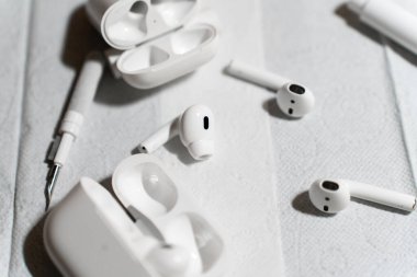 Detaylı bir temizlik işlemi sırasında beyaz bir yüzeye yerleştirilmiş kablosuz kulaklıklar, şarj kutuları ve temizlik aletleri. Görüntü teknik bakım, hijyen ve cihaz bakımını vurguluyor. Yüksek