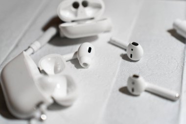 Detaylı bir temizlik işlemi sırasında beyaz bir yüzeye yerleştirilmiş kablosuz kulaklıklar, şarj kutuları ve temizlik aletleri. Görüntü teknik bakım, hijyen ve cihaz bakımını vurguluyor. Yüksek