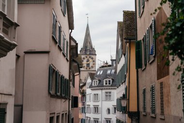 Bulutlu bir gökyüzünün altında tarihi kilise kuleleri ve çatıların yer aldığı panoramik bir Zürih şehri. Görüntü, arka planda dağlar olan İsviçre 'nin eski kasabasının cazibesini yansıtıyor. Yüksek kalite