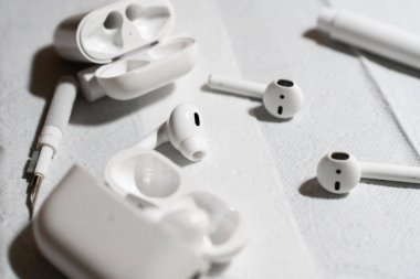 Detaylı bir temizlik işlemi sırasında beyaz bir yüzeye yerleştirilmiş kablosuz kulaklıklar, şarj kutuları ve temizlik aletleri. Görüntü teknik bakım, hijyen ve cihaz bakımını vurguluyor. Yüksek