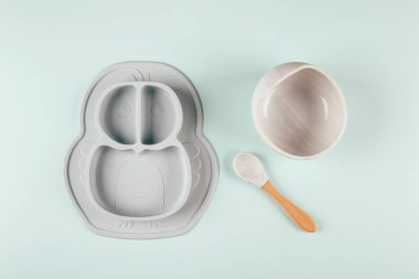 Arka planda gri silikon bulaşık takımı var. Bebeğe hizmet etmek, ilk beslenme konsepti. Düz konum, boşluk kopyala, üst görünüm