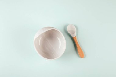 Arka planda gri silikon tabak ve kaşık. Bebeğe hizmet etmek, ilk beslenme konsepti. Düz konum, boşluk kopyala, üst görünüm