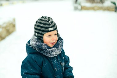 Kar yağışı altında oynayan, kışın giysili, gülümseyen çocuk. Boşluğu kopyala.