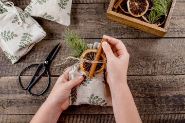 Noel sıfır atık ambalajı. Kuru portakal ve tarçınlı tekstil hediye kesesi dekore eden bir kız. Üst görünüm.