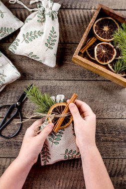 Noel sıfır atık ambalajı. Kuru portakal ve tarçınlı tekstil hediye kesesi dekore eden bir kız..