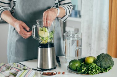 Sağlıklı yeşil meyve püresi yapan bir kadın. Vejetaryen, temiz yeme tarzı konsepti.
