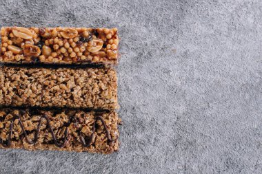 Granola bar. Sağlıklı atıştırmalıklar. Mısır gevreği, fındıklı çikolata, beton masa arkasında çikolata. Kopyalama alanı olan üst görünüm.