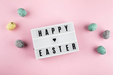 Paskalya bayramı tebrik kartı. Mutlu Paskalyalar yazılı ışık kutusu. Renkli paskalya yumurtaları, tavşanlar. Düz yatış, üst görünüm.