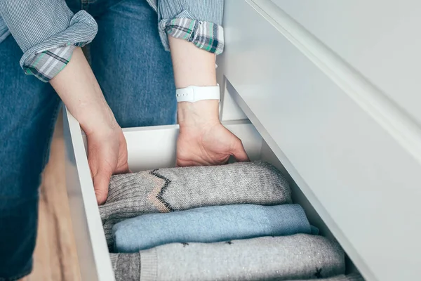 A woman folds clothes sweaters in drawer. Concept of clothes storage, minimalism lifestyle.