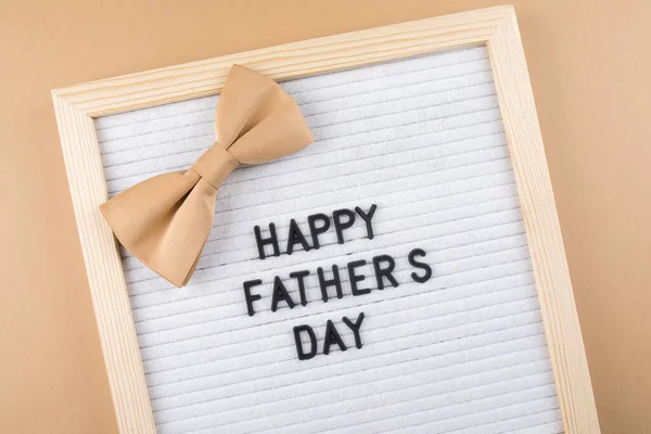 Babalar Günü 'nüz kutlu olsun. Kahverengi arka planda aksesuar erkek kelebeği olan mektup tahtası için tebrikler. Düz yatış, üst görünüm