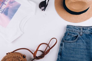 Yaz boyunca hayat devam eder. Sıradan kadın kıyafetleri, aksesuarlar. Tişört, şort, organik rattan çanta, hasır şapka, güneş gözlüğü. Tatil, seyahat konsepti. Üst görünüm düzlüğü