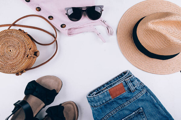 Overhead summer still life. Casual women's clothing, acccessories. Top, shorts, organic rattan bag, straw hat, sandals, sunglasses. Vacation, travel concept. Top view flat lay