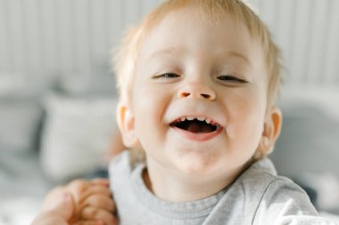 Bir yaşında beyaz bir çocuk kameraya bakıyor ve gülümsüyor. Neşeli çocuk. Otantik insanlar, ev hayatı.