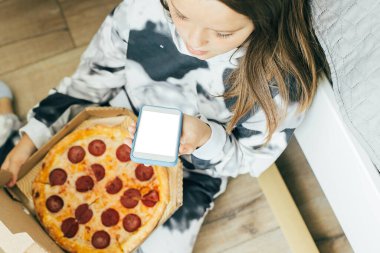 Genç bir kızın evde oturmuş pizza yerken, pepperoni yerken ve sesli mesaj kaydederken görüntüsü çok güzel.