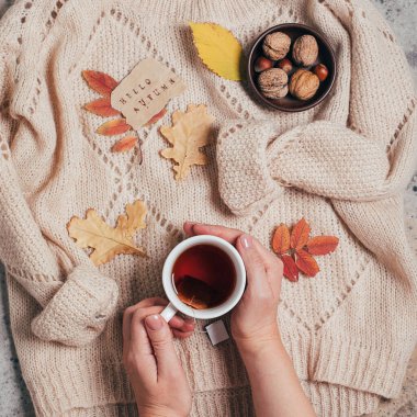 Sıcak siyah çay, kazak, fındık ve sonbahar yaprakları tutan kadın elleri. Sonbahar rahatlama kavramı.