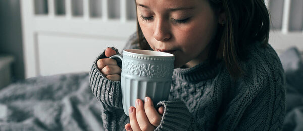 Молодая девушка пьет горячий шоколад на уютной кровати в спальне. Концепция осенних или зимних выходных, Знамя для дизайна, веб-страница