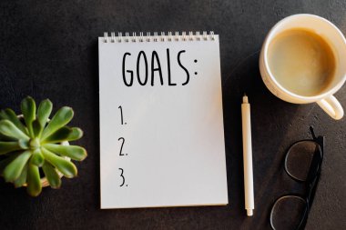 Defterde 2026 gol. Lezzetli bir bitki, bir fincan kahve, koyu renkli bir masa. Üst manzara, düz uzanma