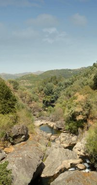 Dağ nehri manzarası, kayaların ortasında küçük bir gölet ve güneşlenen insanlar, yaz ve sıcak, tatiller ve eğlence.
