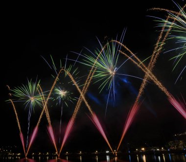 Havai fişeklerin farklı stilleri, havada sıkışmış ateş, menekşe, yeşil ve mavi renkler, suda yansımalar