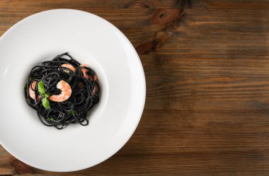 Siyah İtalyan deniz ürünleri makarnası, beyaz restoran tabağında karides ve ahşap zemin üzerinde fotokopi alanı. Siyah ev yapımı spagetti, mürekkepbalıklı erişte, pişmiş deniz makarnası.
